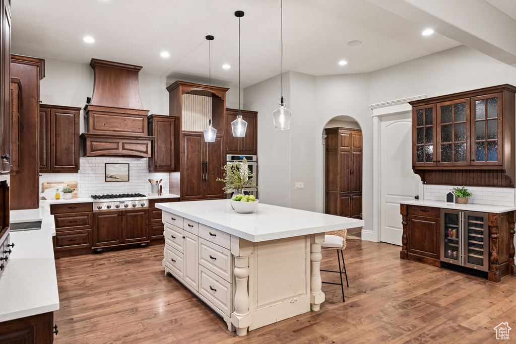 Kitchen with wine cooler, arched walkways, custom exhaust hood, light countertops, and dark brown cabinetry