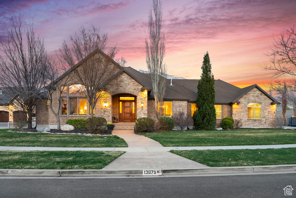 French country inspired facade featuring stone siding, brick siding, a yard, and roof with shingles