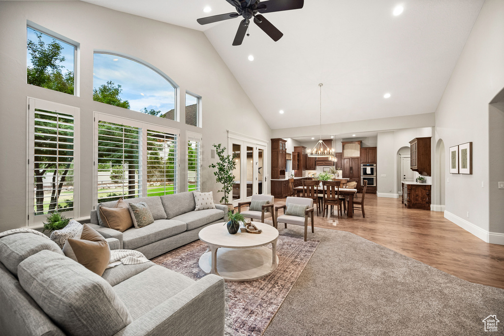 Living room featuring high vaulted ceiling, ceiling fan, a chandelier, arched walkways, and light wood-style floors