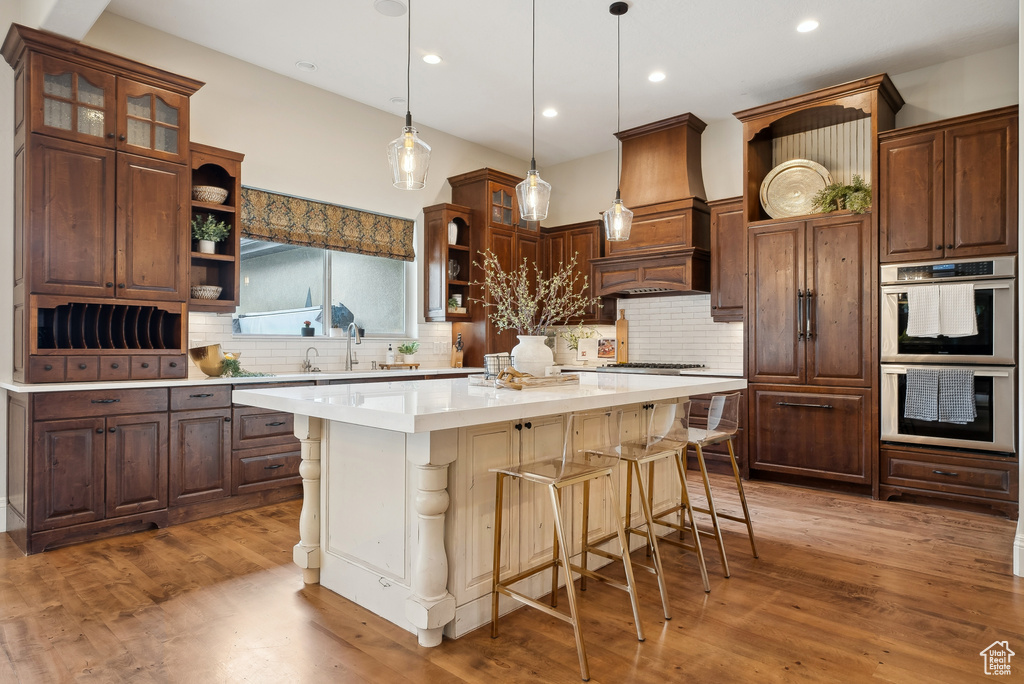 Kitchen with open shelves, stainless steel double oven, a breakfast bar area, decorative backsplash, and recessed lighting