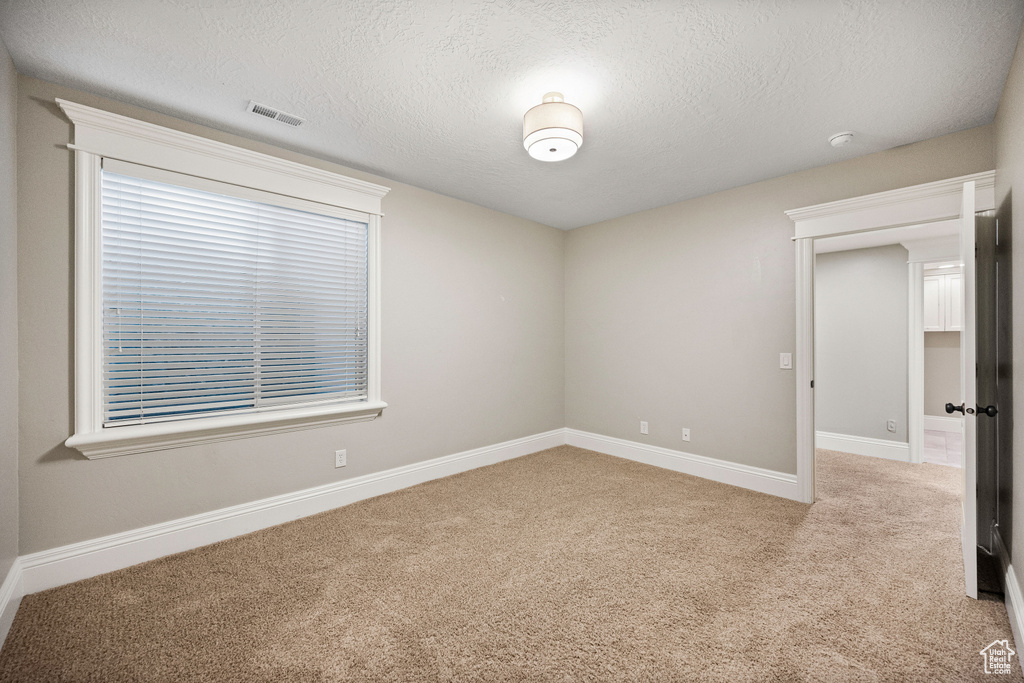 Spare room featuring light carpet, a textured ceiling, and a smoke detector