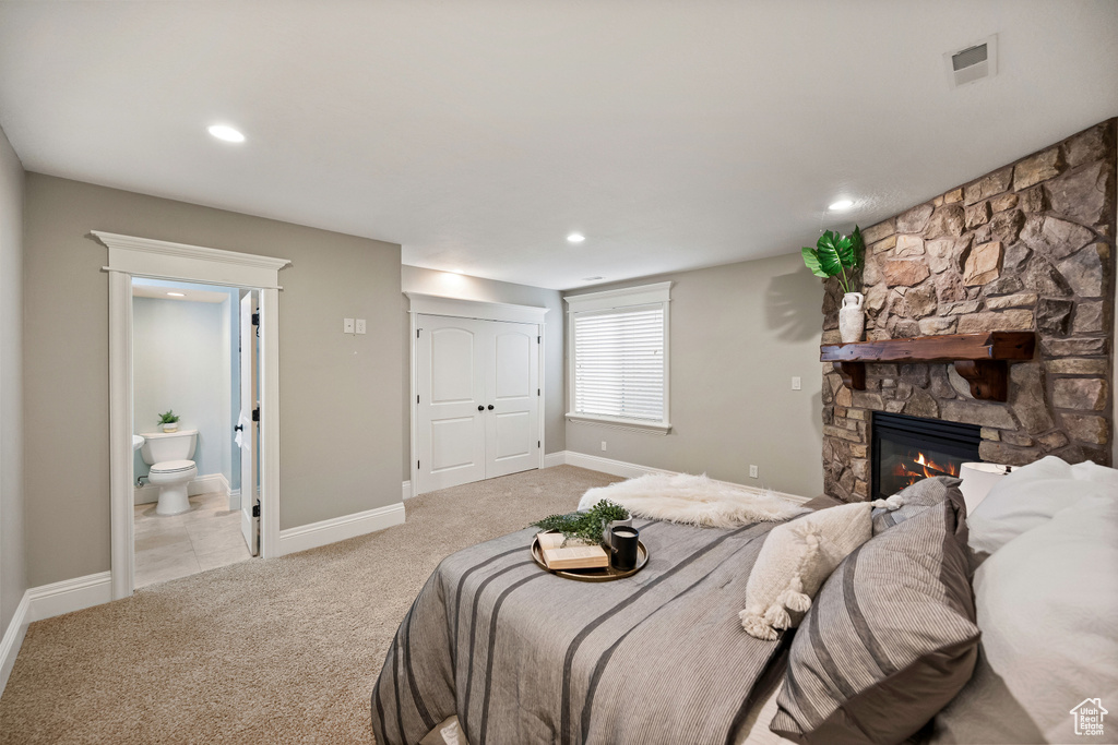 Bedroom featuring light carpet, recessed lighting, a stone fireplace, and ensuite bath