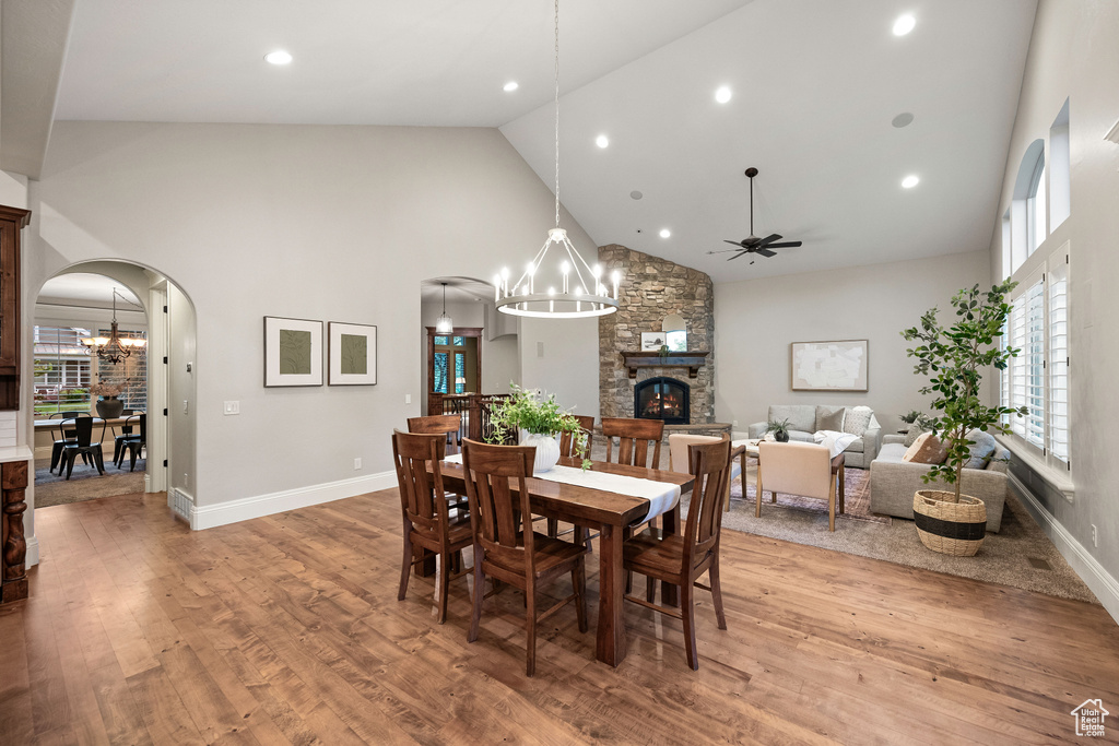 Dining room featuring high vaulted ceiling, a fireplace, arched walkways, a chandelier, and a ceiling fan