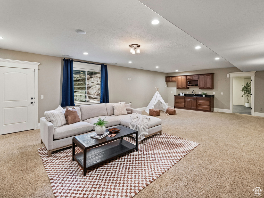 Living area featuring light carpet, recessed lighting, and bar with sink
