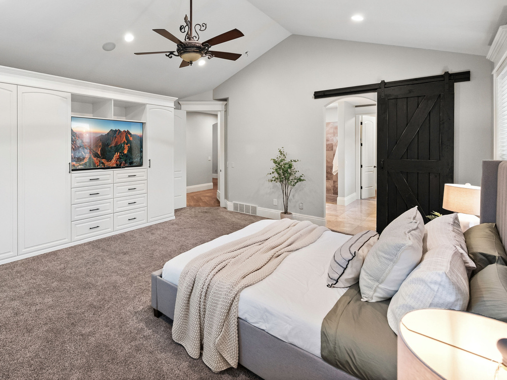 Bedroom with a barn door, vaulted ceiling, recessed lighting, light carpet, and a ceiling fan