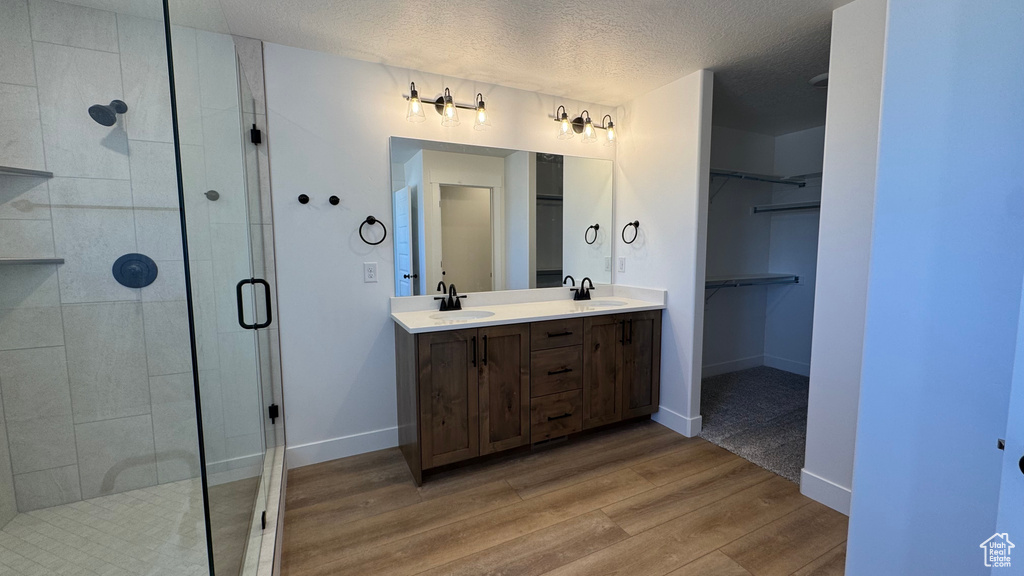 Bathroom featuring a stall shower, wood finished floors, a textured ceiling, a spacious closet, and double vanity