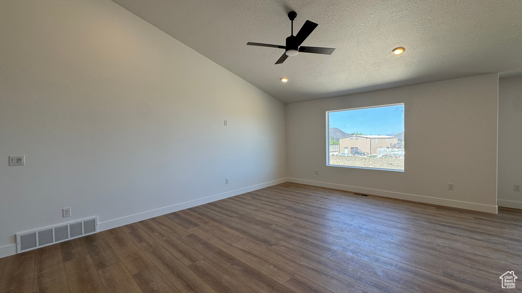 Empty room with a textured ceiling, a ceiling fan, lofted ceiling, dark wood-type flooring, and baseboards