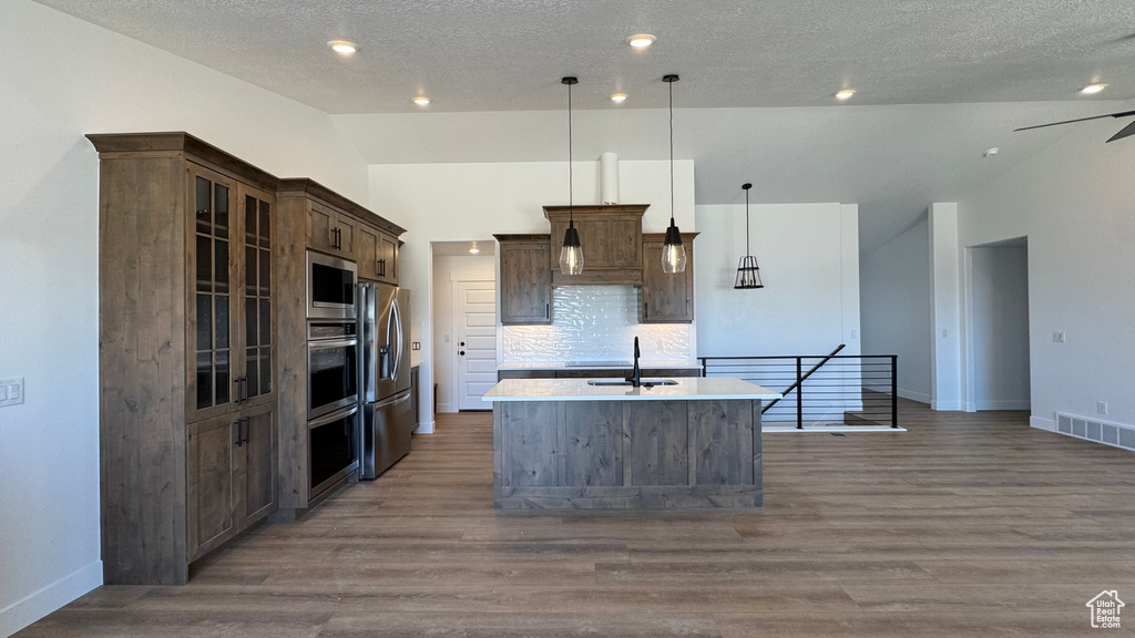 Kitchen with vaulted ceiling, a center island with sink, stainless steel appliances, a sink, and wood finished floors