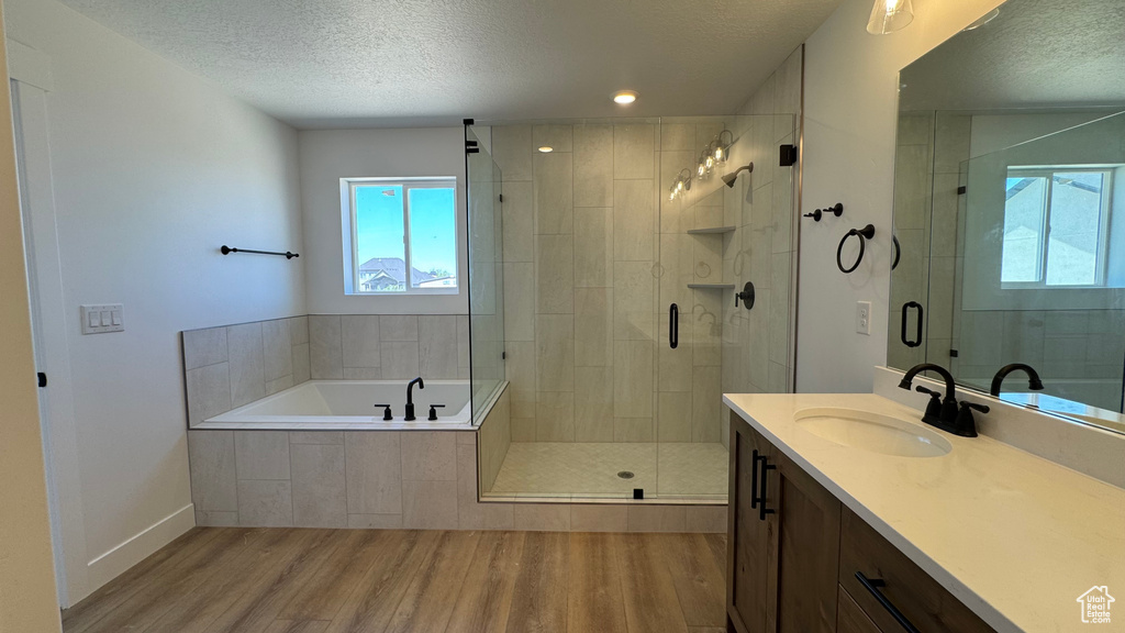 Full bath with wood finished floors, a textured ceiling, vanity, a stall shower, and a garden tub