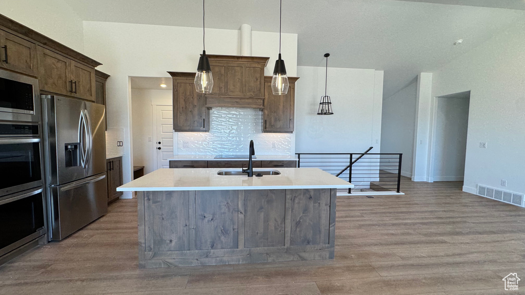 Kitchen with appliances with stainless steel finishes, a sink, light wood-style flooring, and a kitchen island with sink
