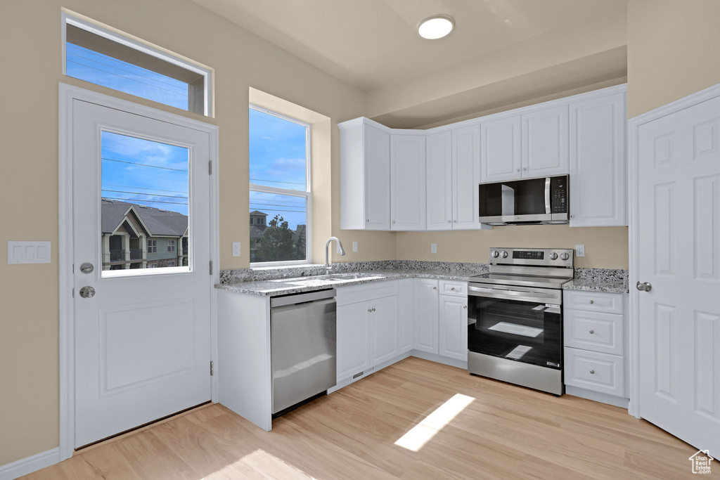 Kitchen with stainless steel appliances, light wood finished floors, white cabinets, and light stone counters