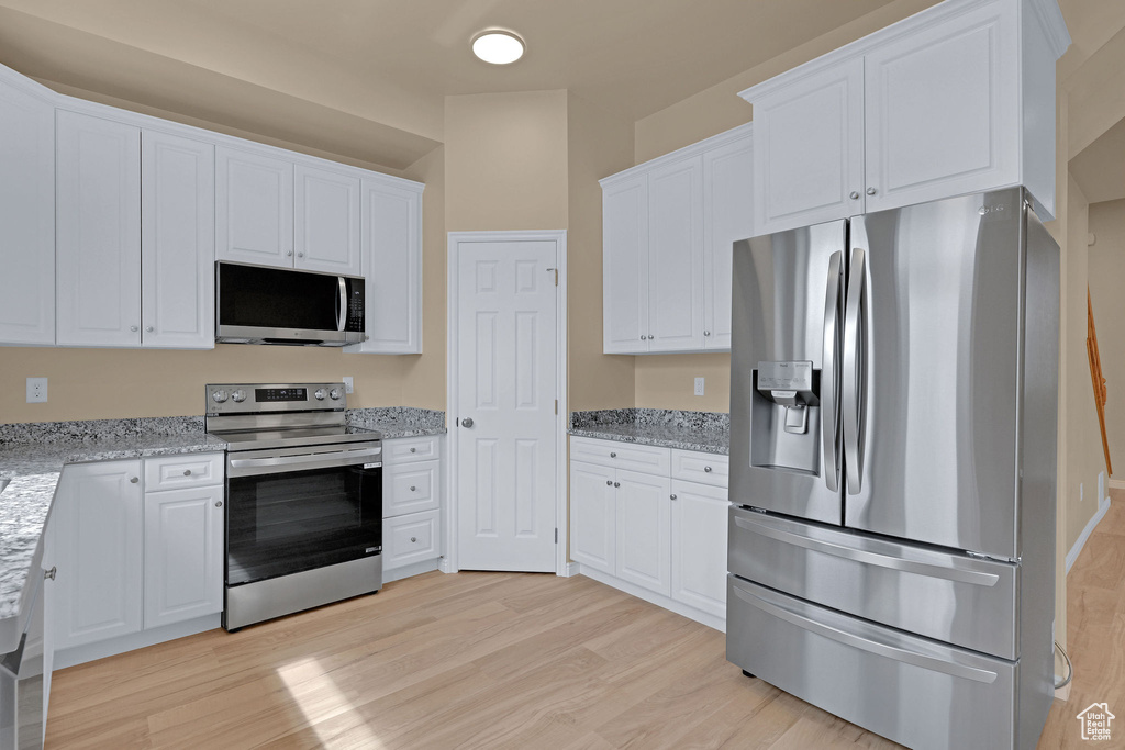 Kitchen with light wood finished floors, white cabinets, and stainless steel appliances