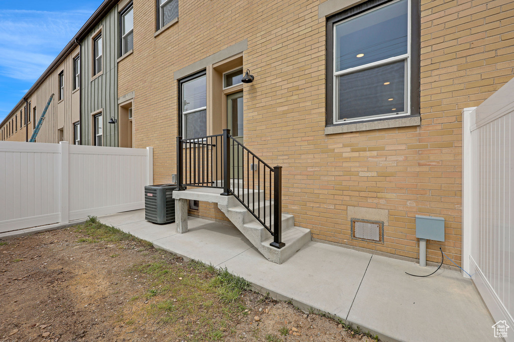Property entrance with brick siding, crawl space, fence, and central AC unit