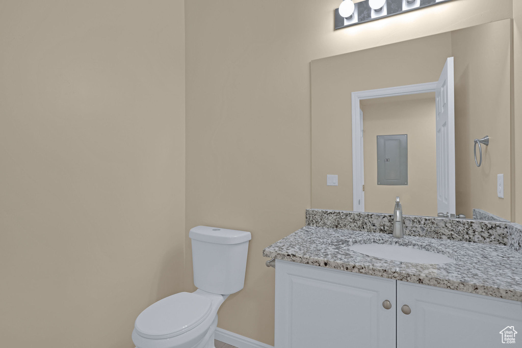 Half bathroom with electric panel, vanity, baseboards, and toilet