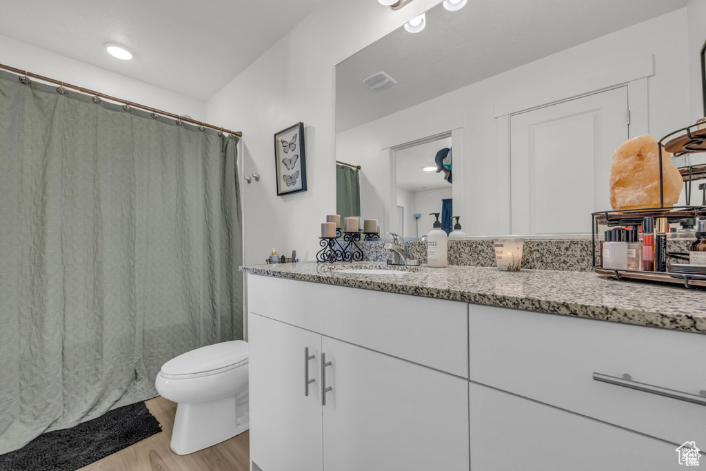 Full bathroom with vanity, a shower with curtain, visible vents, toilet, and wood finished floors