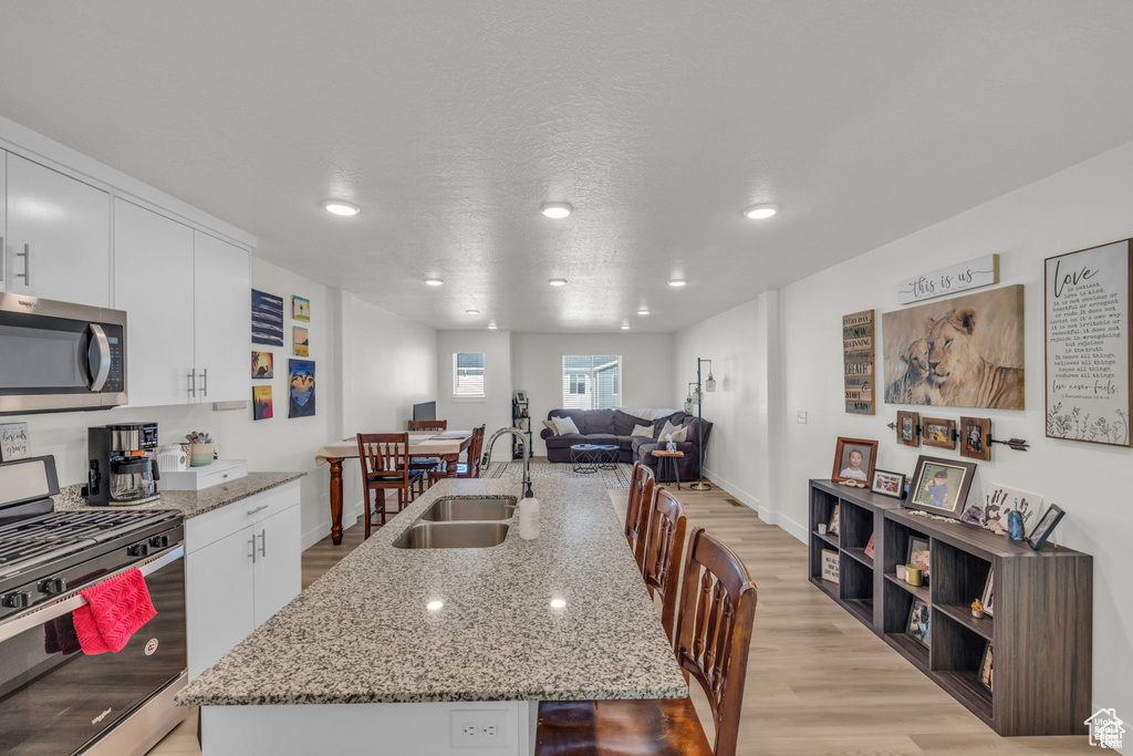 Kitchen with white cabinets, a center island with sink, stainless steel appliances, light wood finished floors, and a sink