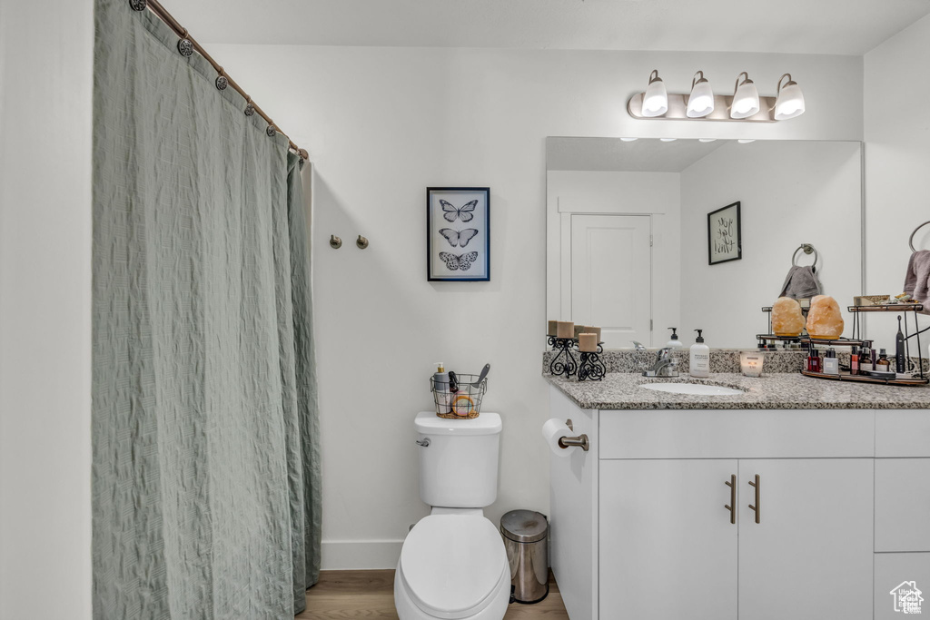 Full bath with baseboards, a shower with curtain, toilet, vanity, and wood finished floors
