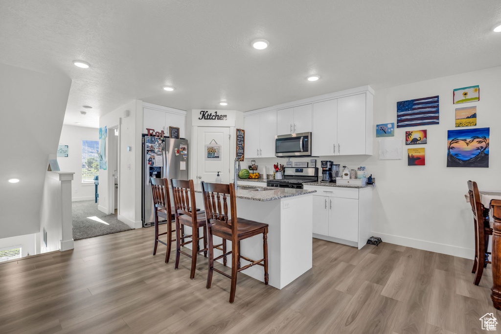 Kitchen featuring a center island, a sink, appliances with stainless steel finishes, light wood-style flooring, and a breakfast bar area