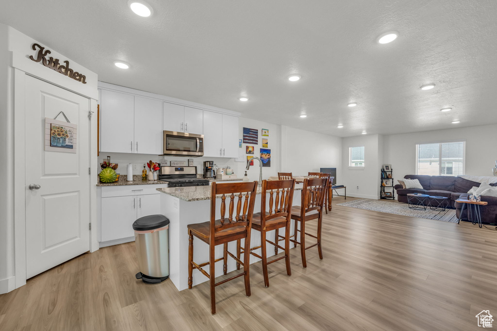 Kitchen featuring open floor plan, white cabinets, light wood-style floors, a kitchen bar, and appliances with stainless steel finishes