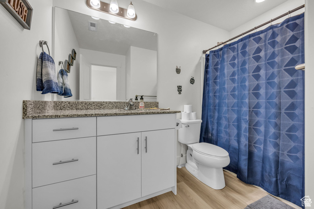 Bathroom featuring a shower with shower curtain, vanity, toilet, visible vents, and wood finished floors