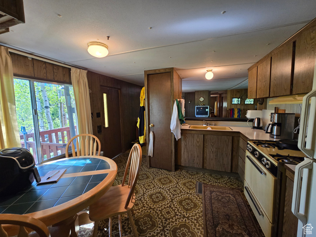 Kitchen with gas range gas stove, wood walls, brown cabinets, tile countertops, and a sink