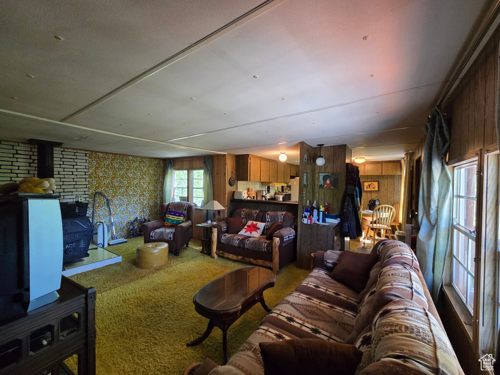 Carpeted living area featuring a wood stove, wooden walls, and wallpapered walls
