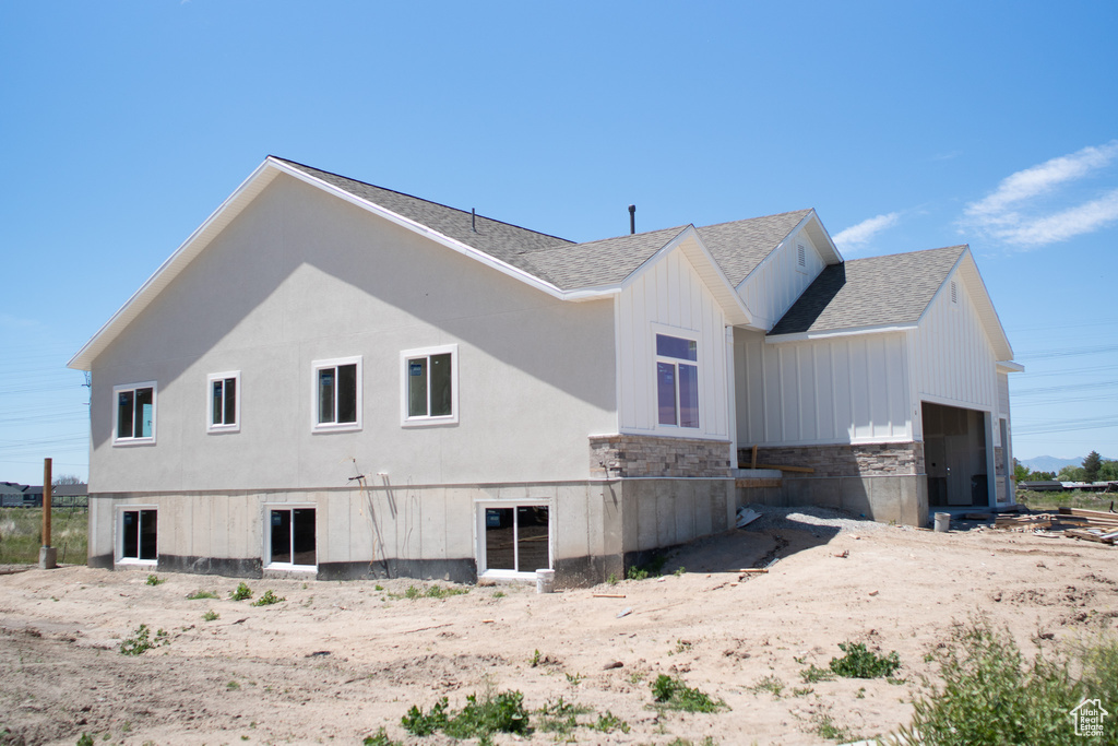 View of side of home with a shingled roof, stone siding, a garage, and board and batten siding