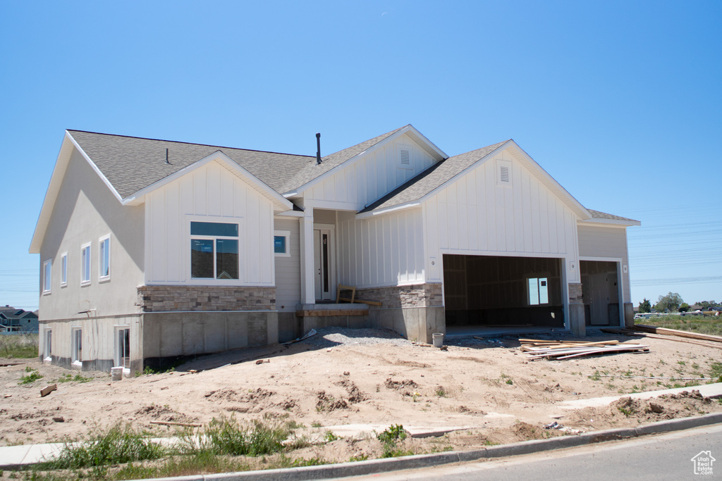 Modern farmhouse style home with a shingled roof, board and batten siding, an attached garage, and stone siding