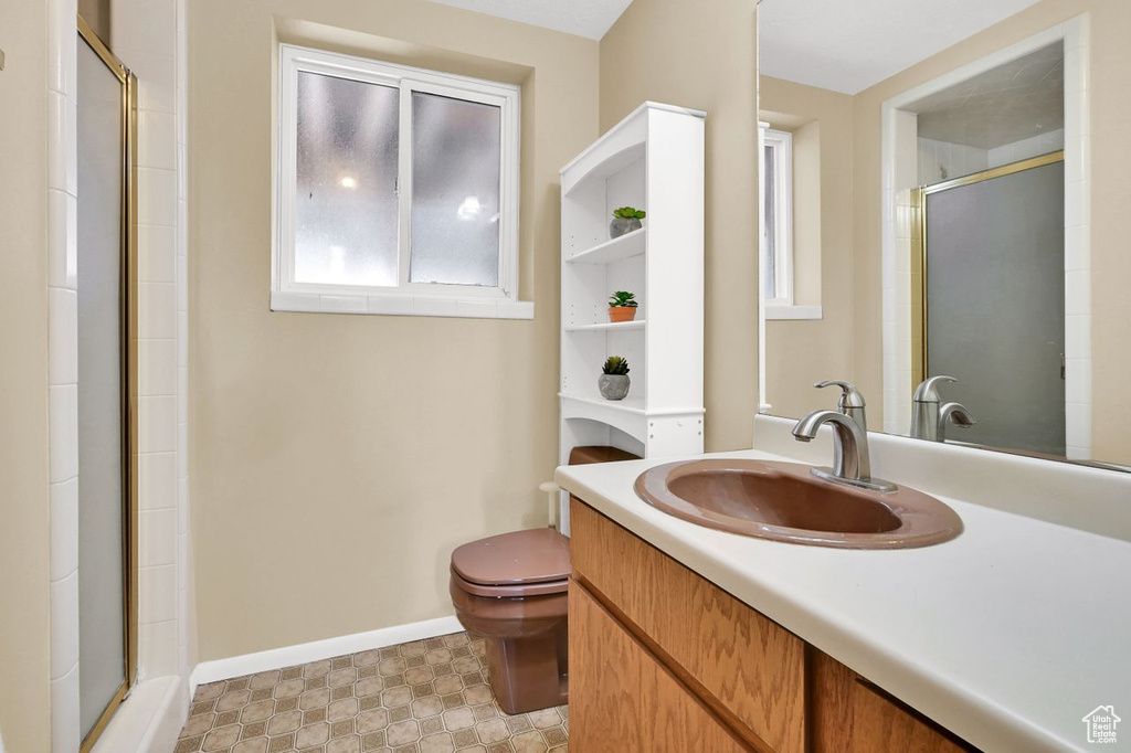 Bathroom featuring a shower with door, vanity, baseboards, and toilet