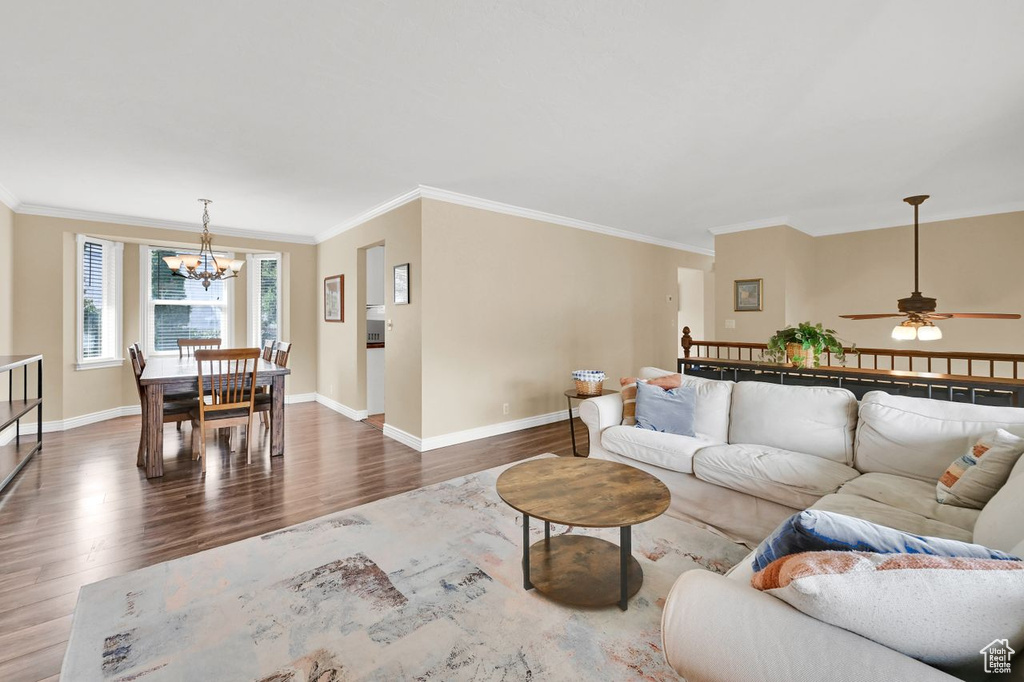 Living area with ceiling fan with notable chandelier, baseboards, crown molding, and wood finished floors