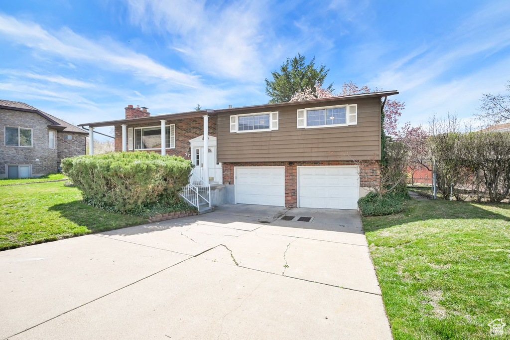 Split foyer home featuring brick siding, a front yard, driveway, and a garage