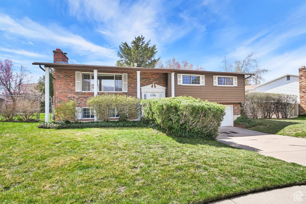 Bi-level home featuring a chimney, concrete driveway, a front yard, and brick siding