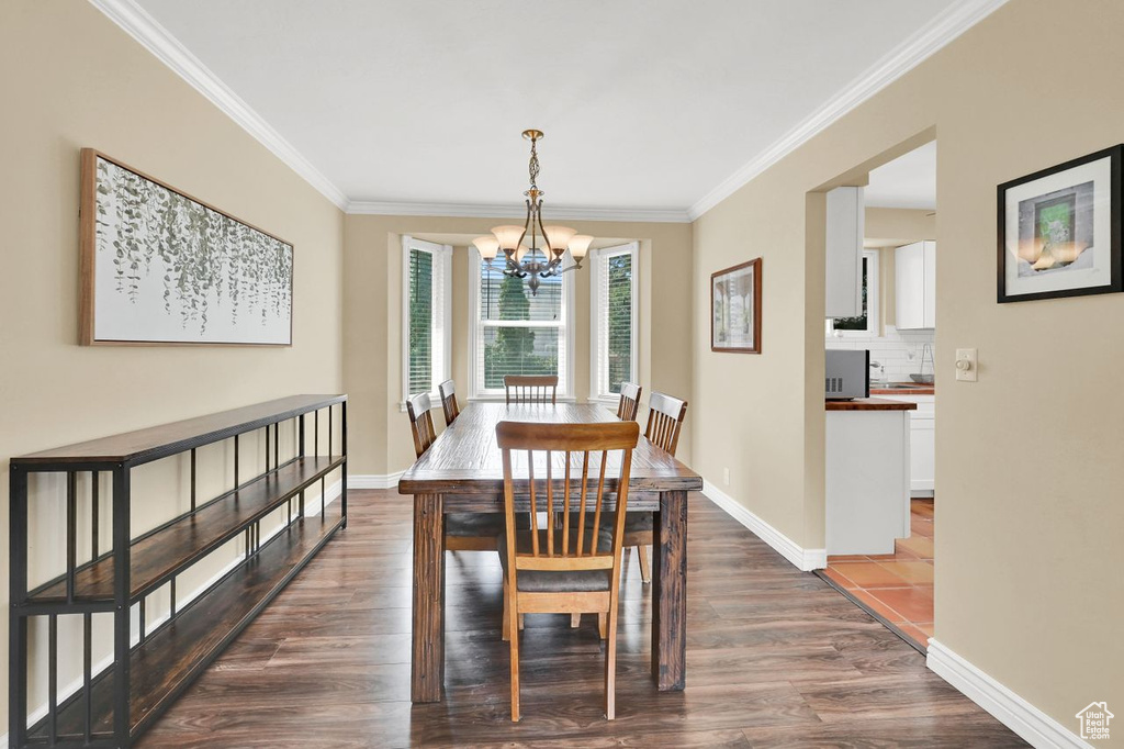 Dining area featuring dark wood-style flooring, ornamental molding, baseboards, and an inviting chandelier