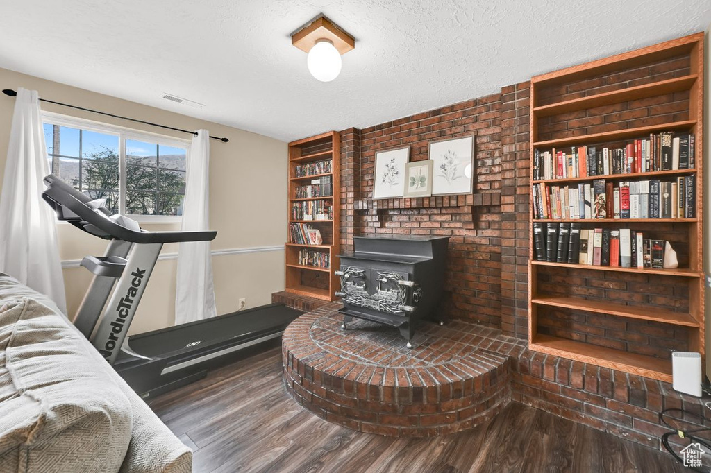 Interior space featuring visible vents, built in shelves, a wood stove, a textured ceiling, and wood finished floors