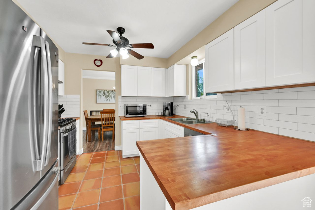 Kitchen featuring a ceiling fan, appliances with stainless steel finishes, light tile patterned flooring, a sink, and wooden counters