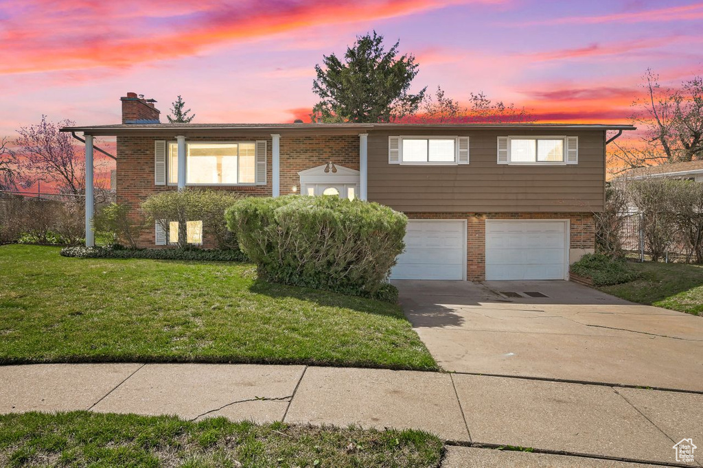 Split foyer home with a chimney, driveway, an attached garage, brick siding, and a lawn