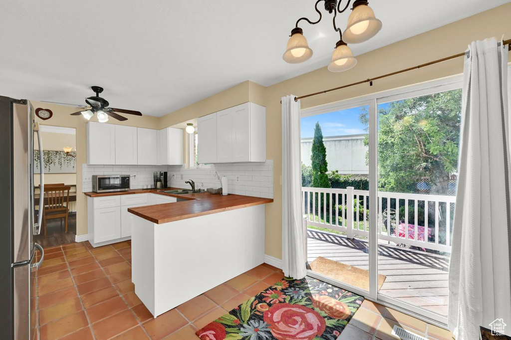 Kitchen featuring a peninsula, white cabinetry, decorative backsplash, stainless steel appliances, and a sink