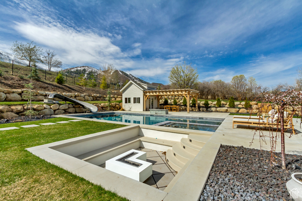 Outdoor pool featuring a water slide, a pergola, a patio area, an outdoor fire pit, and a mountain view