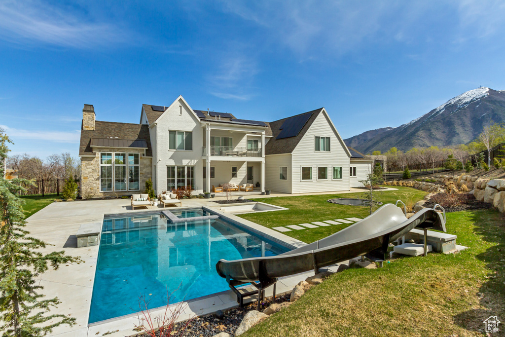 Rear view of house with a balcony, roof mounted solar panels, a patio area, a mountain view, and stone siding