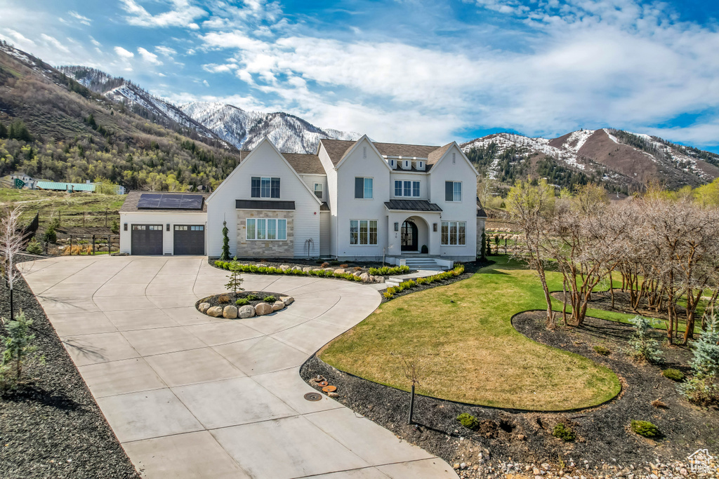 View of front facade with curved driveway, a mountain view, an attached garage, roof mounted solar panels, and a front lawn