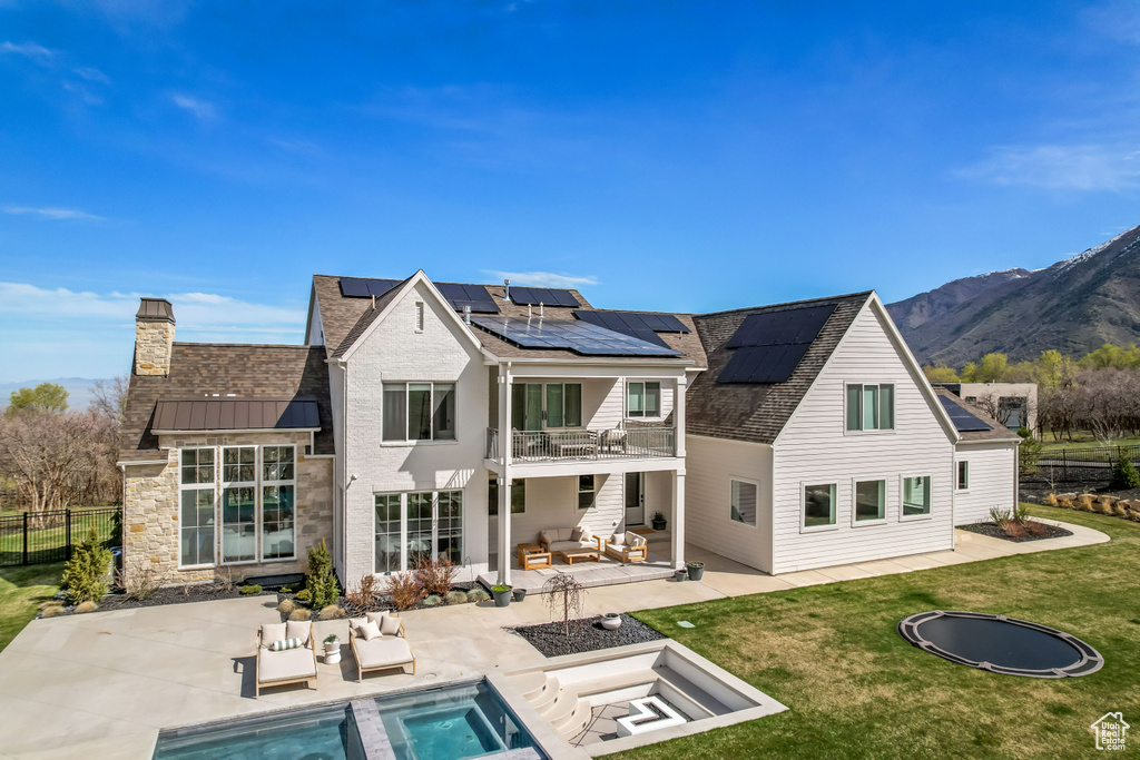 Back of house featuring an outdoor living space, a balcony, a patio, an in-ground hot tub, and roof mounted solar panels