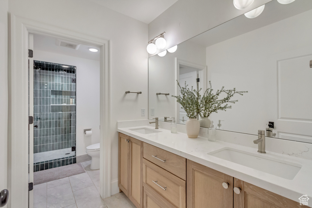Bathroom with toilet, double vanity, and tiled shower
