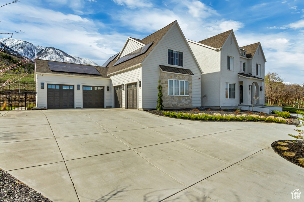 View of front of property featuring concrete driveway, a mountain view, solar panels, and a shingled roof