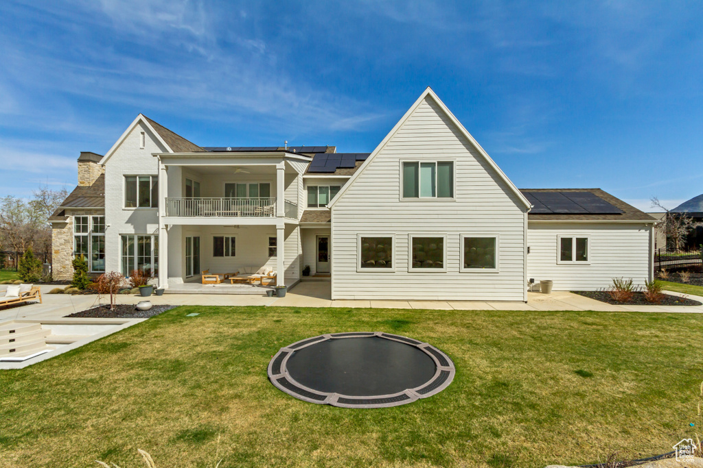 Rear view of house with a balcony, a patio area, and roof mounted solar panels