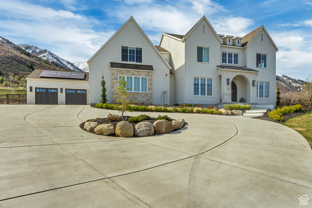 View of front of home with curved driveway, solar panels, a mountain view, stone siding, and stucco siding