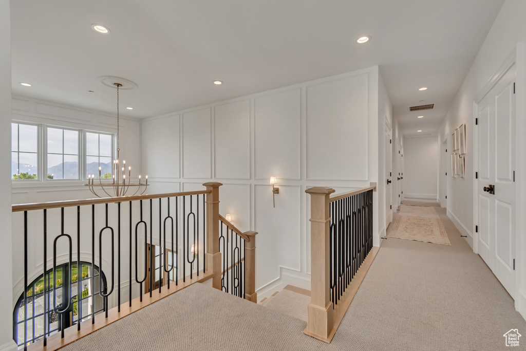 Hall featuring a decorative wall, a chandelier, recessed lighting, an upstairs landing, and light colored carpet