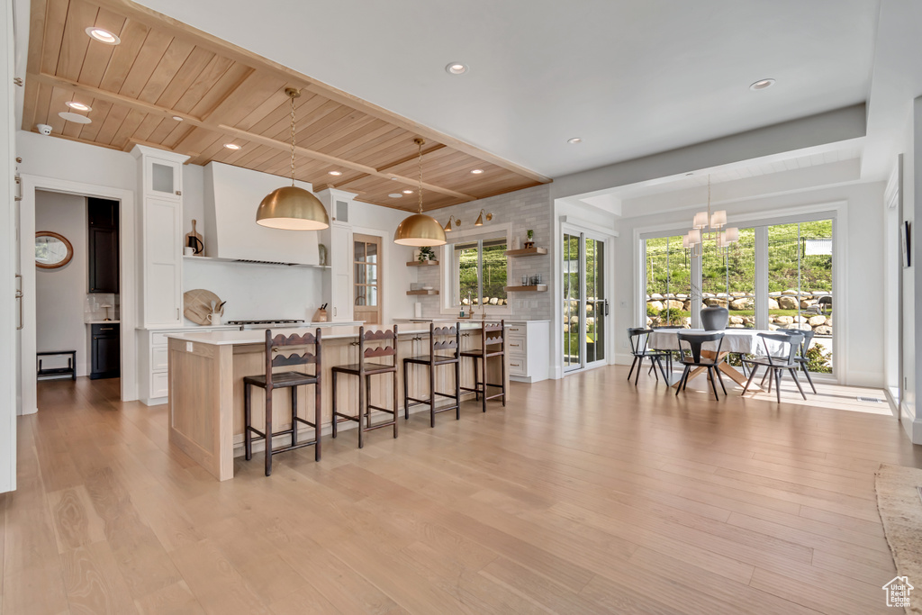 Kitchen with open shelves, a breakfast bar area, light countertops, wooden ceiling with exposed beams, and light wood-type flooring