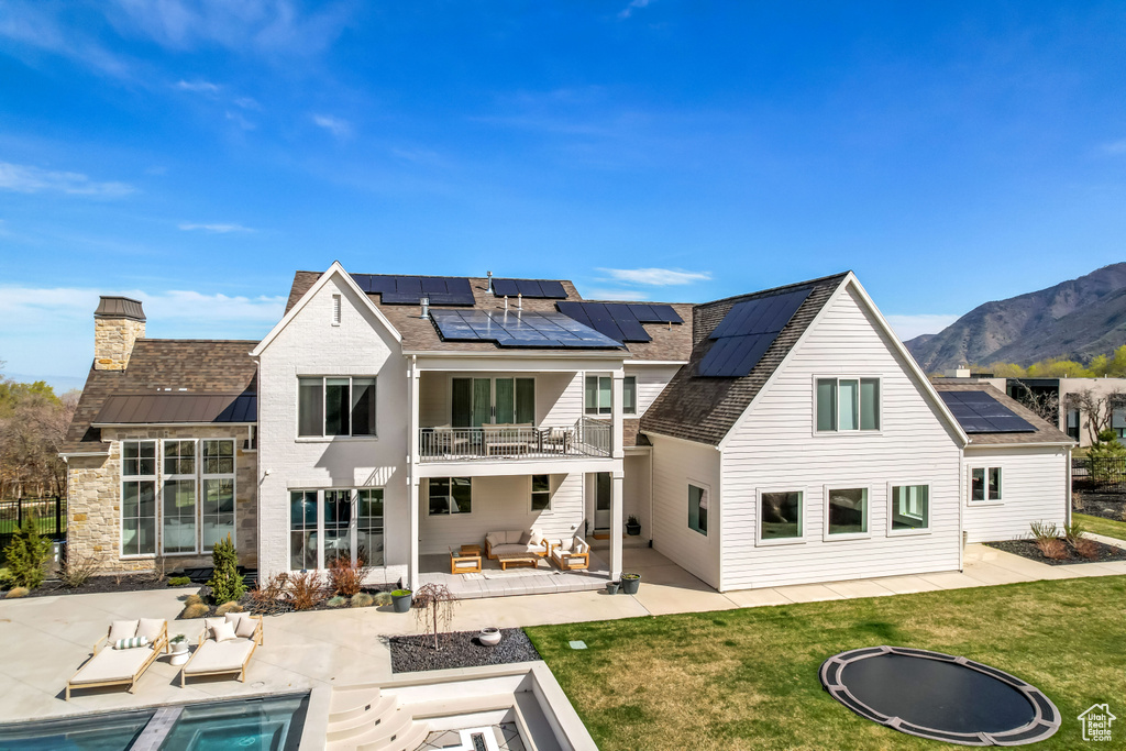 Rear view of property featuring a balcony, an outdoor living space with a fire pit, a patio area, roof mounted solar panels, and a yard