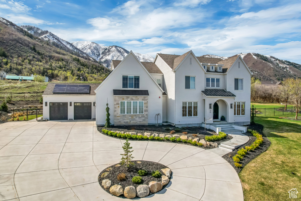 View of front facade with a mountain view, a standing seam roof, roof mounted solar panels, and curved driveway
