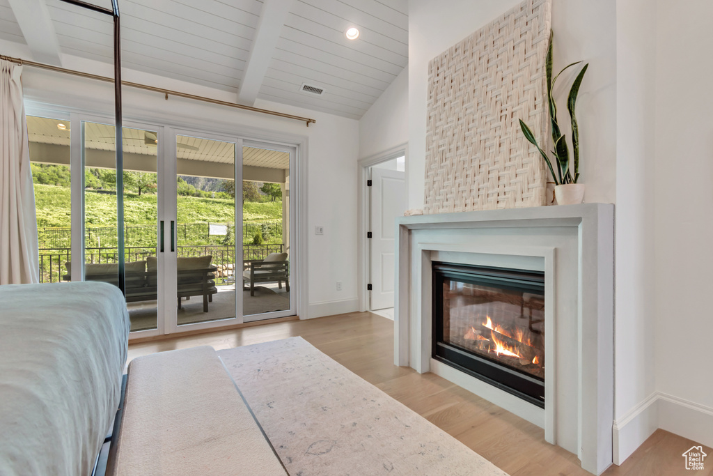 Bedroom featuring access to outside, wood finished floors, baseboards, a glass covered fireplace, and wooden ceiling